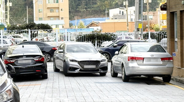 거 차량이 지나는 좁은 골목 코너에서 주차금지선에 주차한 차량 사이로 승용차가 간신히 지나가고 있다